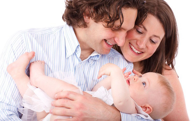brown haired couple looking down while father is holding the baby