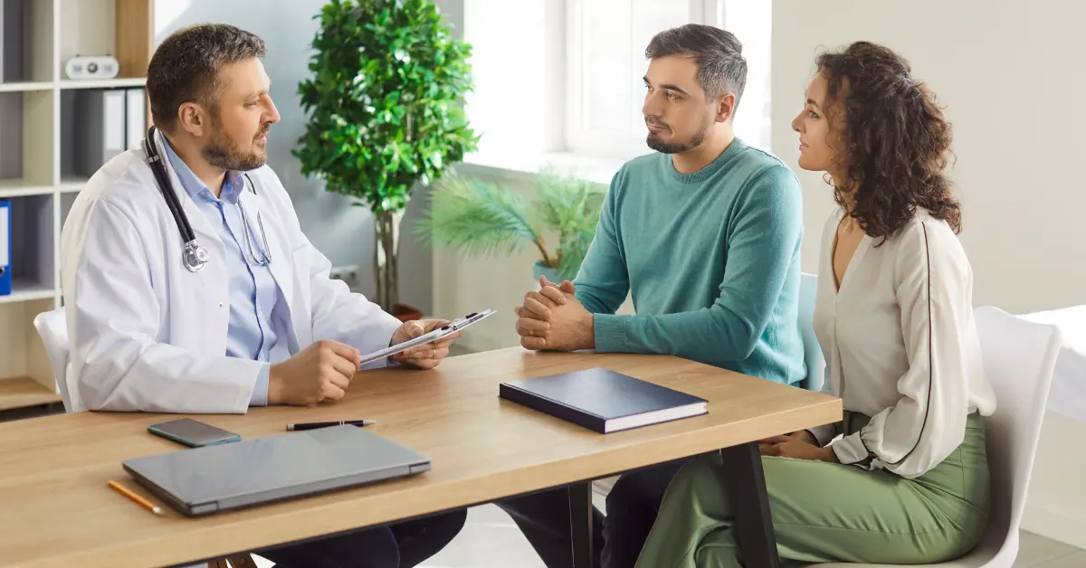 Infertility treatment options explained by a smiling doctor to a hopeful couple during a fertility consultation.