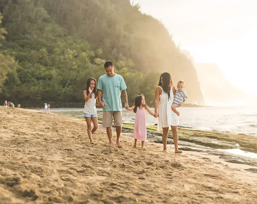 A family of five holding hands and walking along a sunset beach