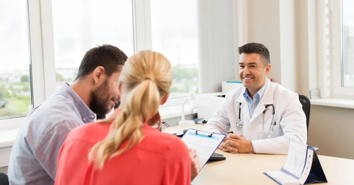 Fertility doctor smiling while consulting a couple in a bright medical office