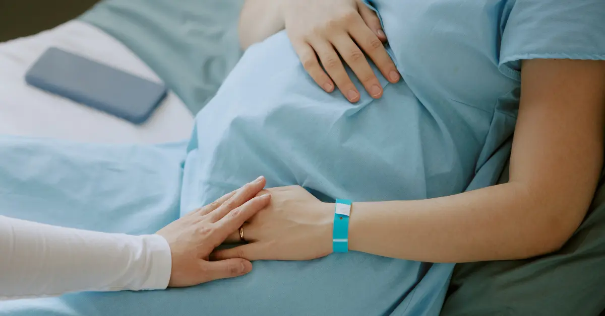Fertility treatment after 40 represented by a pregnant woman lying in a hospital bed with a supportive hand on her belly.
