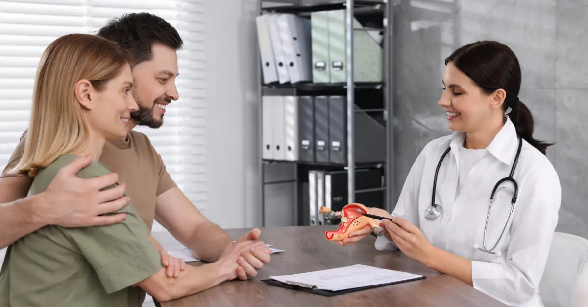 Fertility treatments consultation showing couple with female doctor holding anatomical model of female reproductive system.