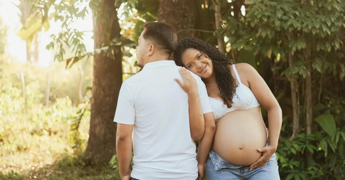 In vitro fertilization success shown by a smiling pregnant woman holding her belly next to her partner outdoors.