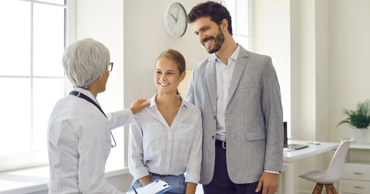 IVF fertility treatment preparation discussion between smiling couple and older doctor in bright medical office