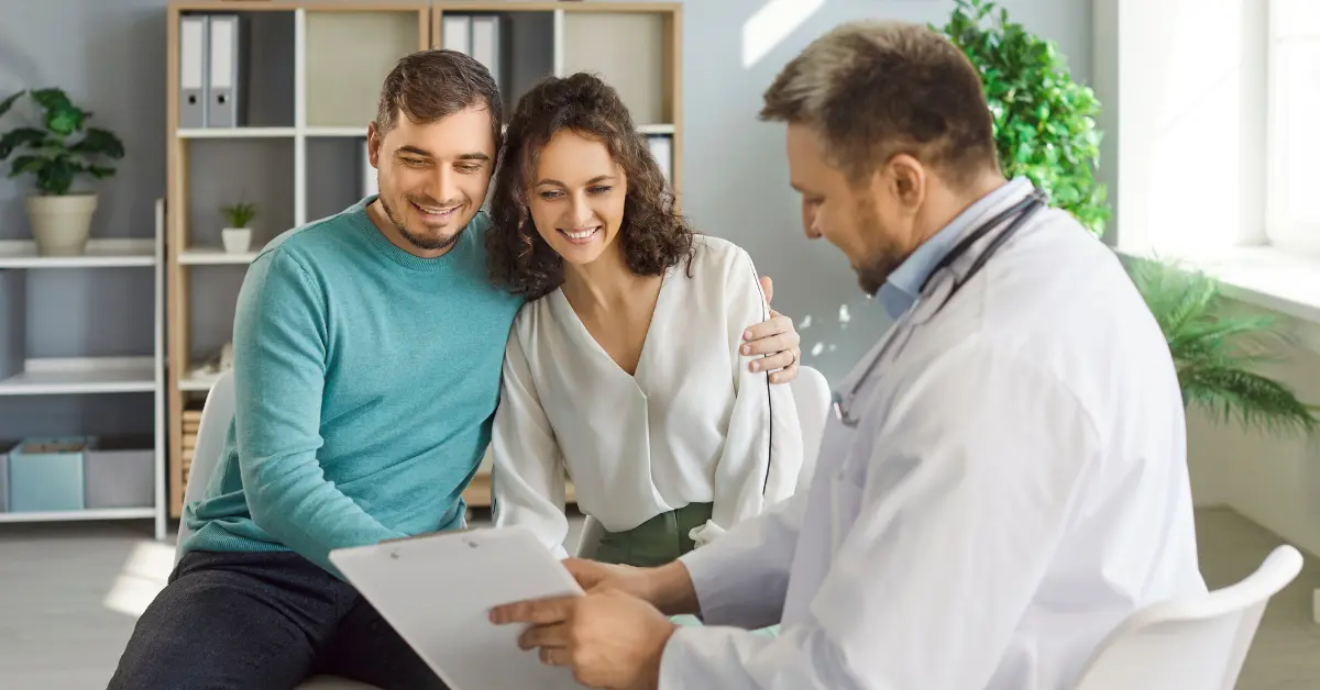 Uterine fibroid treatment options reviewed by a doctor showing paperwork to a smiling couple in an office.