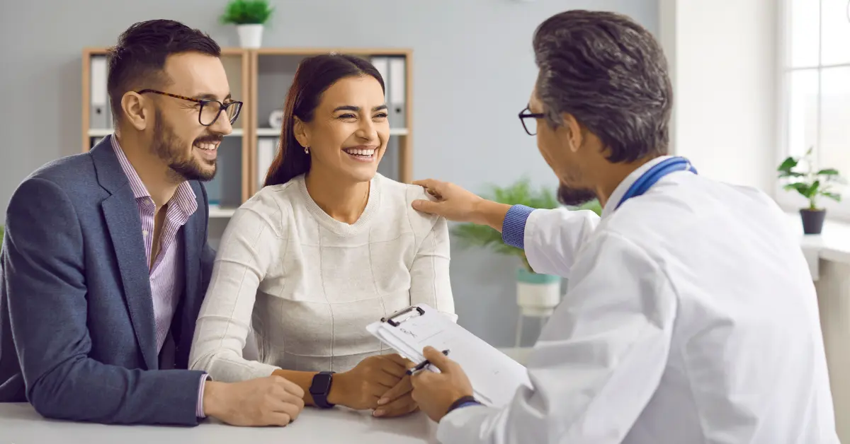 Intracytoplasmic sperm injection consultation with a smiling couple and supportive doctor during a fertility appointment.